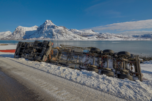 semi truck turned on its side on a snowy road with mountains and a lake in the background