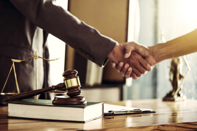 people shaking hands over a desk with a gavel and books