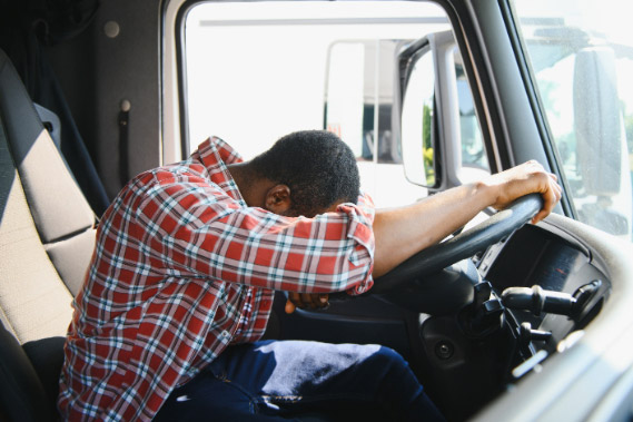 Tired Truck Driver Sitting in Cab Resting Head on Steering Wheel