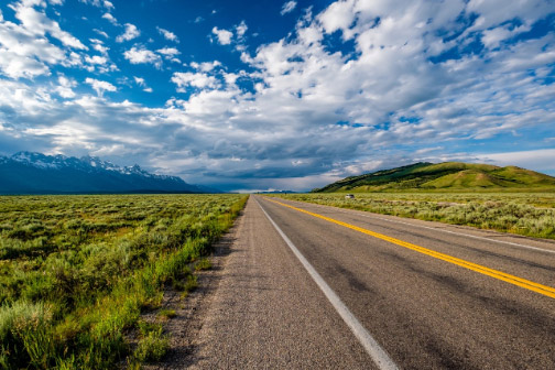 Wyoming Open Highway Road with Green Fields and Cloudy Blue Skies