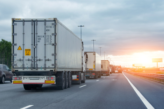 semi trucks in a row in the left lane with a sunset in the distance