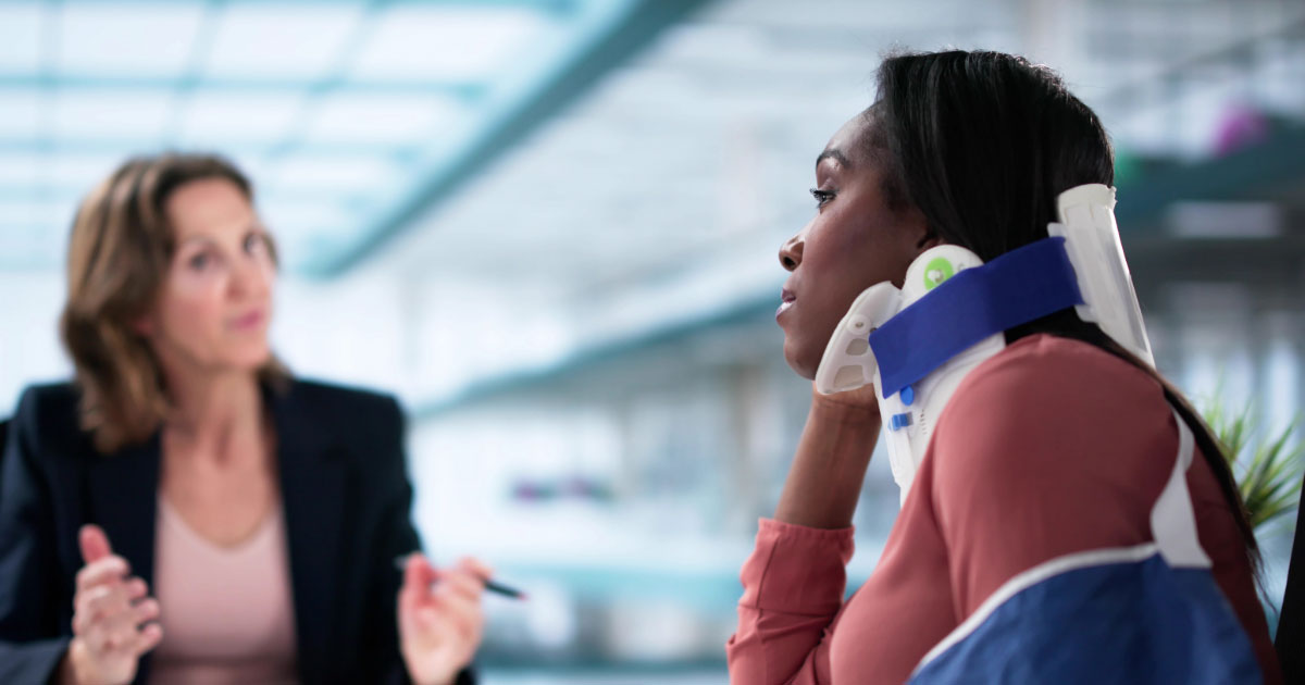 Woman wearing neck brace and cast speaking with lawyer
