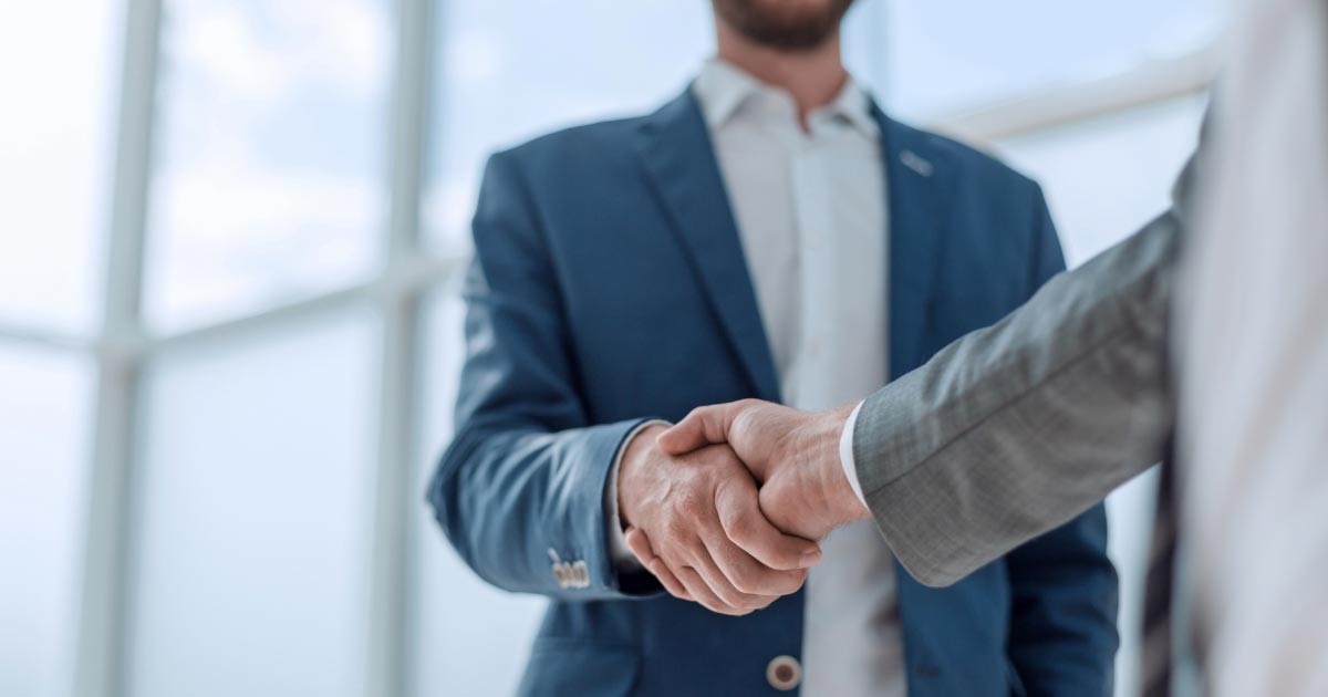 Two men wearing business casual wear shaking hands
