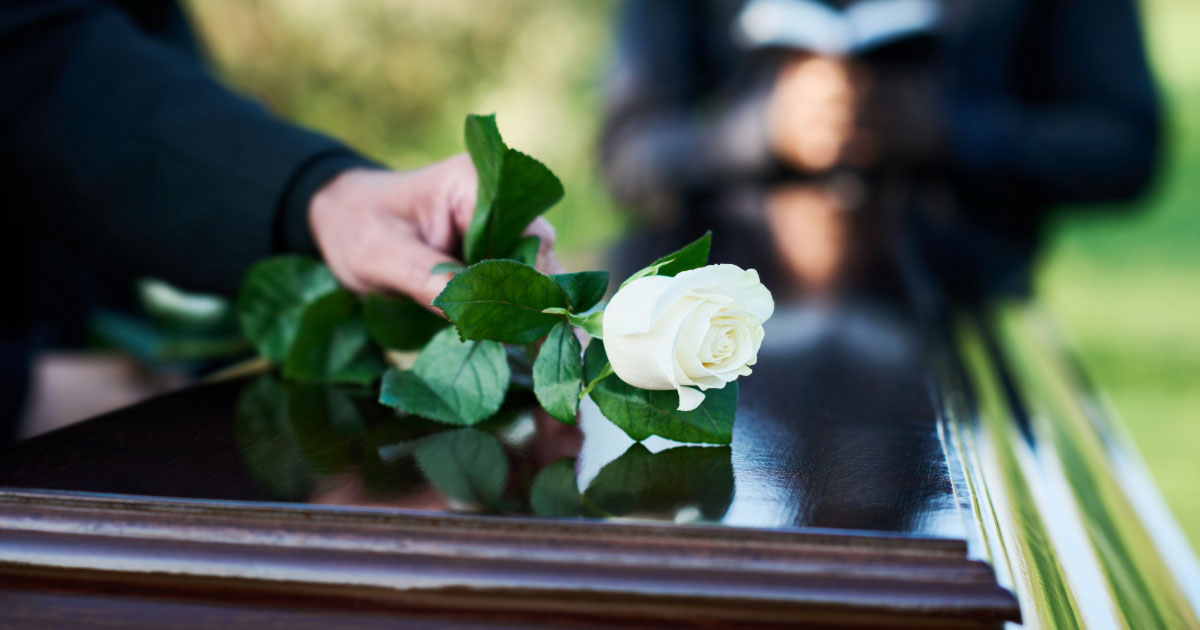 Woman placing a single white rose on top of a wooden casket at a funeral