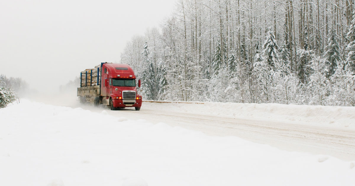Logging truck driving along ice covered highway